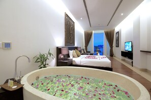 Ein modernes Hotelzimmer mit einer großen Badewanne, einem Bett mit weißer Bettdecke, einem Fernseher und Blick auf die Stadt.