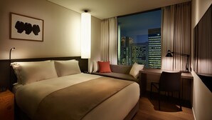 A hotel room with a large bed, a desk, and a view of a cityscape at night.