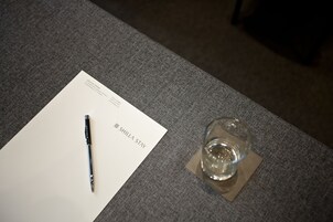 A white business card with "SHILLA STAY" text, a pen, and a glass of water on a grey textured surface.