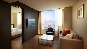 A modern hotel room with a bed, a sofa, a coffee table, and a TV.