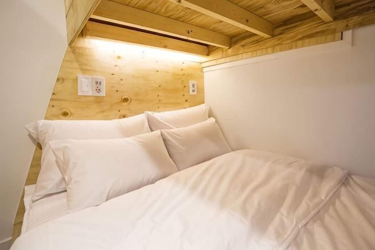 A bedroom with a wooden ceiling, a bed with white bedding, and a white wall.