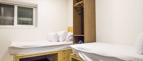 A small, clean room with two single beds, a wooden wardrobe, and a window.