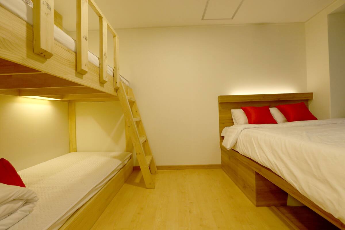 A room with bunk beds and a ladder, wooden walls, and a wooden floor.