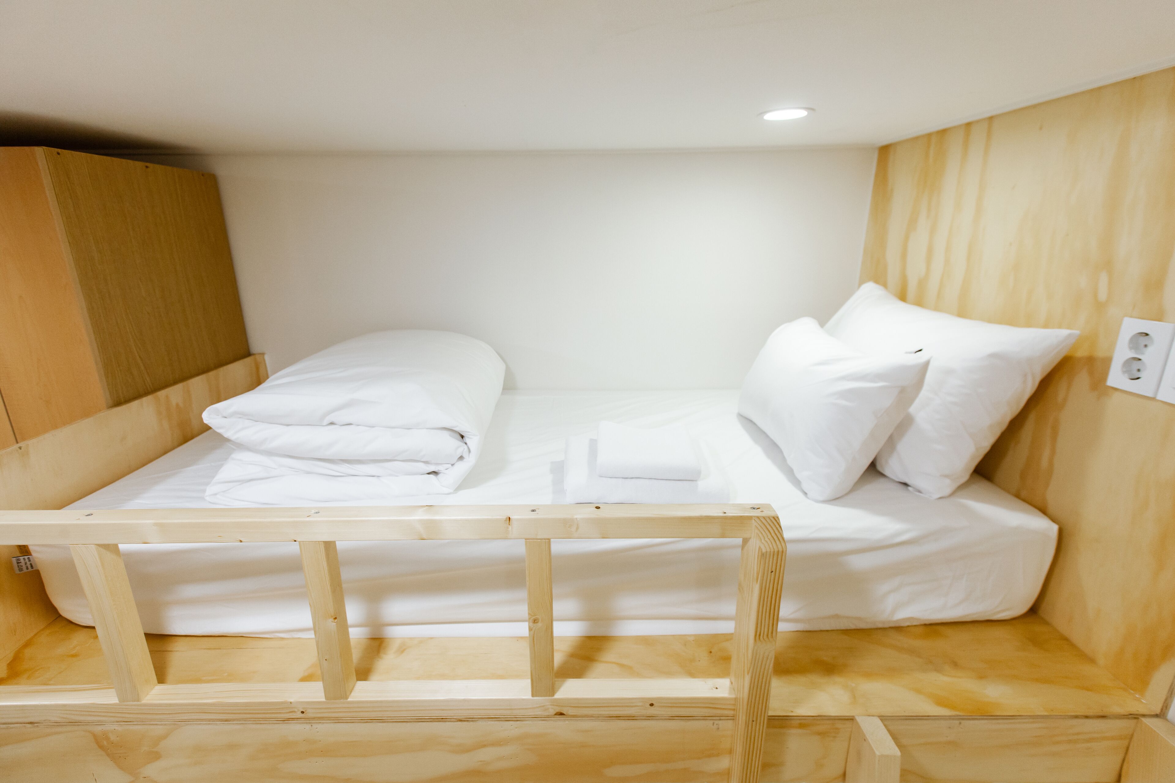 A wooden bunk bed with white bedding and pillows, a wooden headboard, and a wall socket.
