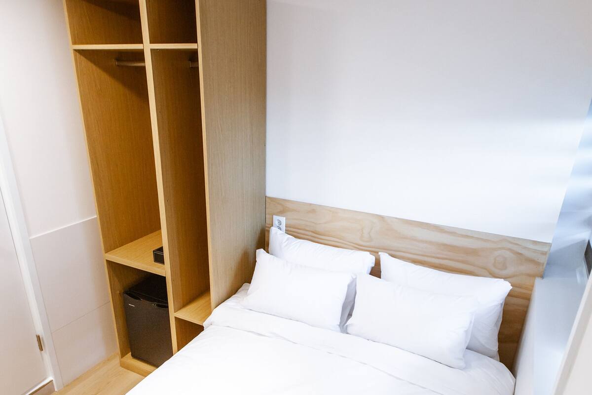 A bedroom with a bed, white bedding, a wooden headboard, and a built-in wardrobe.