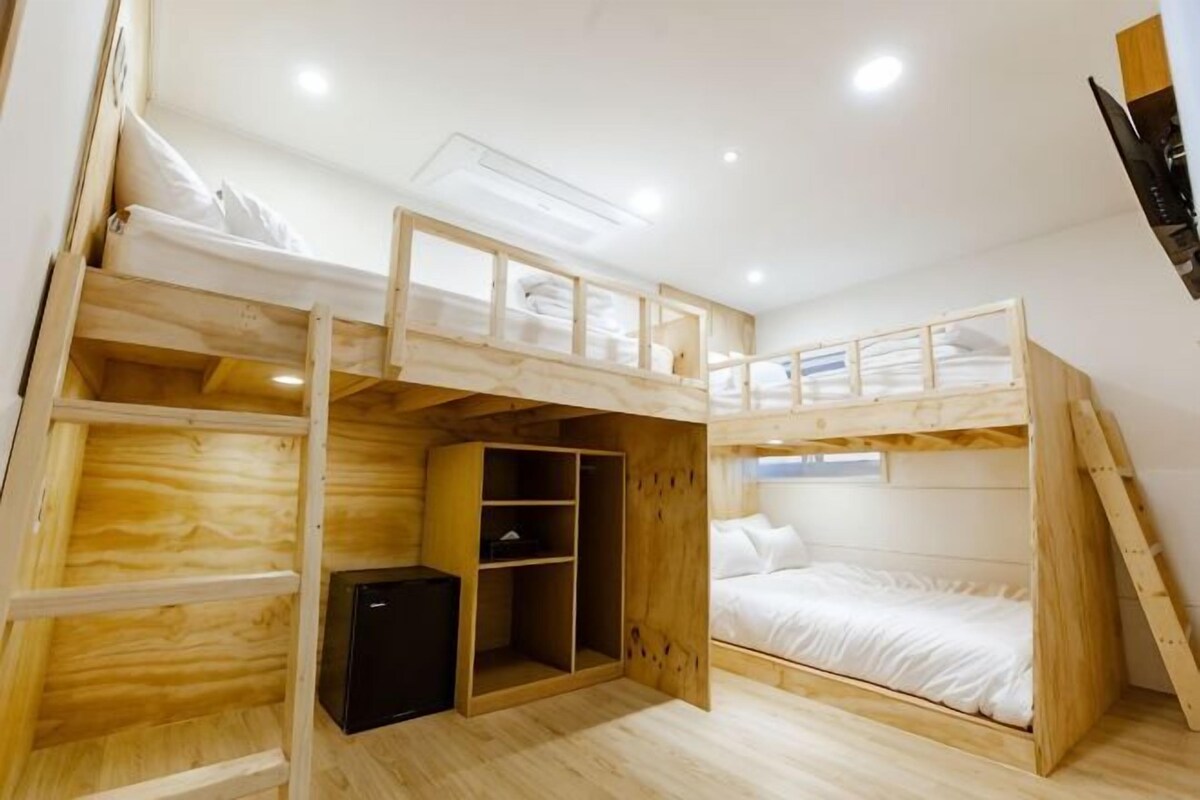 A bunk bed room with a wardrobe, a small desk, and a window.