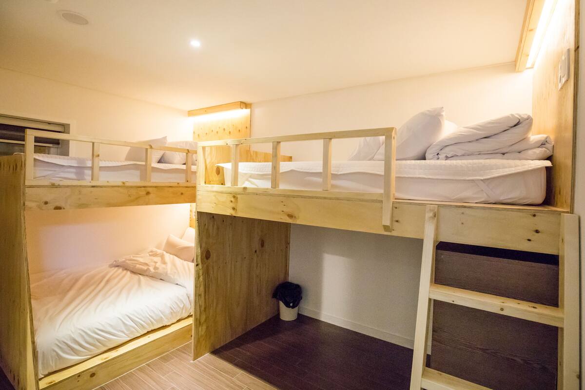 A bunk bed room with a wooden headboard, a small trash bin, and a ceiling light.