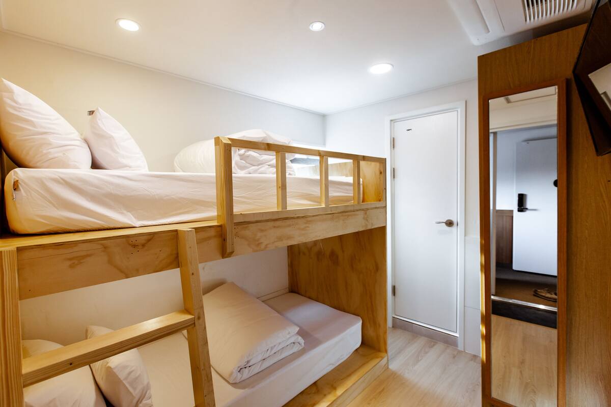 A bunk bed room with a wooden headboard, a white door, and a small kitchenette area.