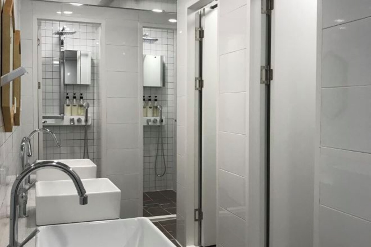 A modern bathroom with a white sink, a mirror, and a shower area.