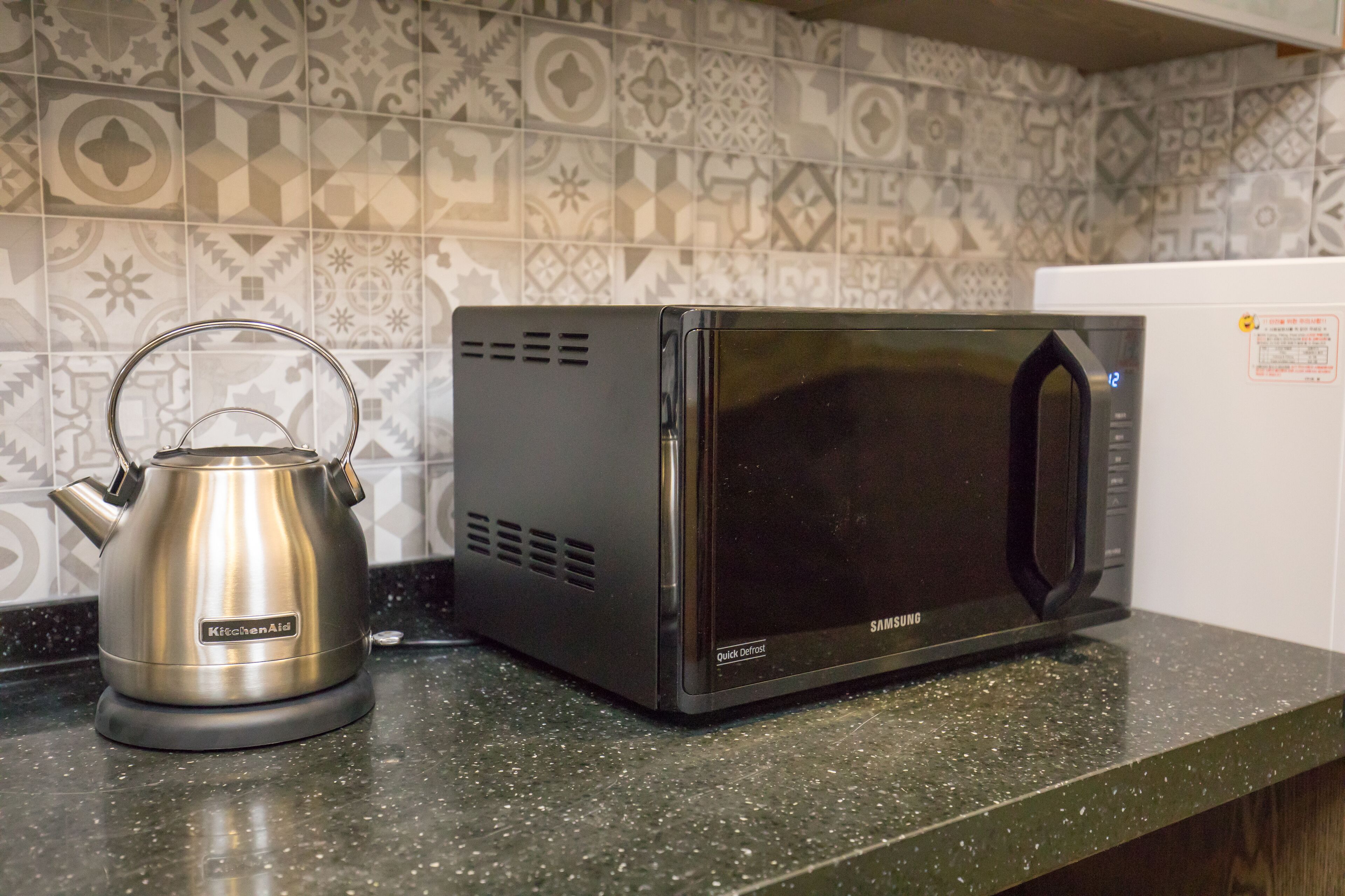 Een keuken met een waterkoker en een magnetron op een gemarmereerd aanrecht.
