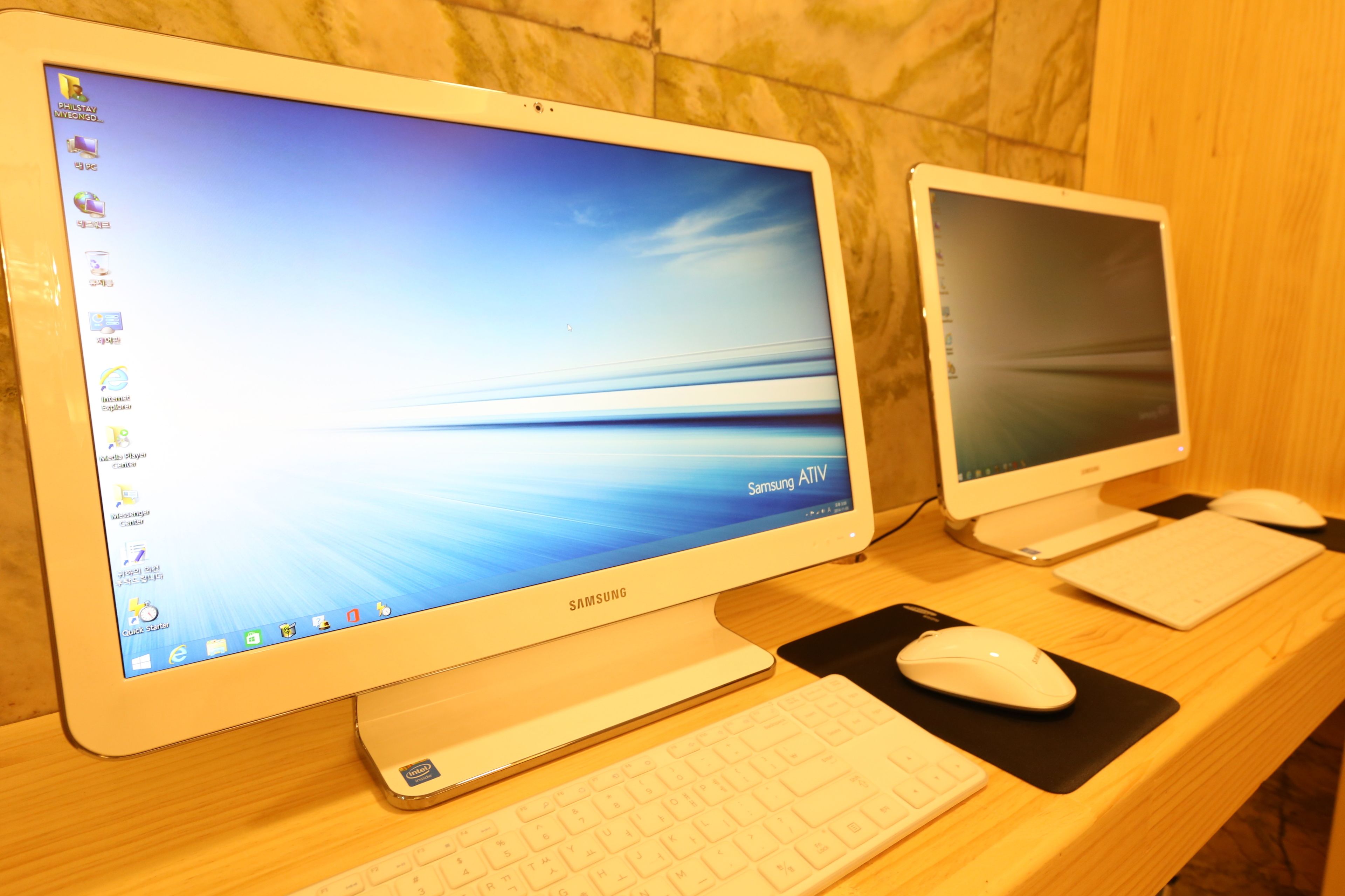 Dos monitores Samsung sobre un escritorio de madera, uno con teclado y ratón, y el otro con un ratón.