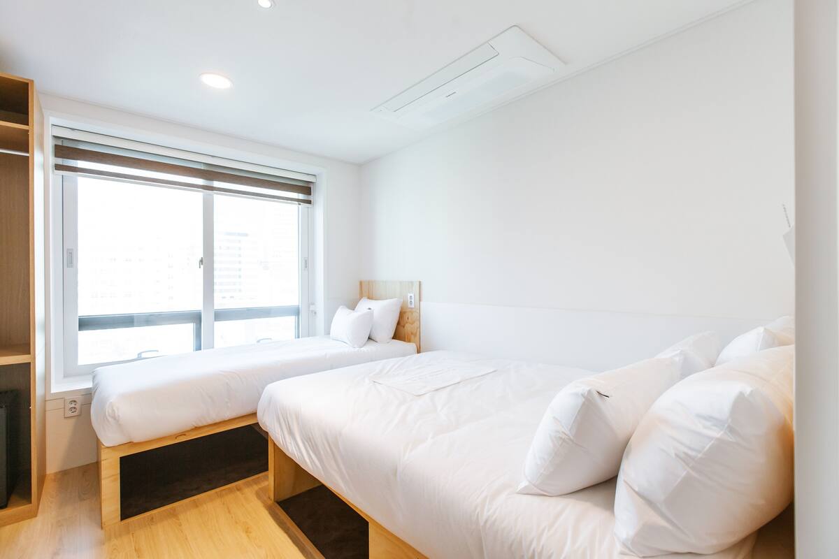 A modern hotel room with two beds, a large window, and a built-in wardrobe.