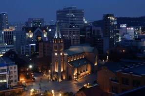 A cityscape at dusk with a prominent church featuring a tall steeple and a large, illuminated building in the background. - Step Inn Myeongdong 1 (Seoul)