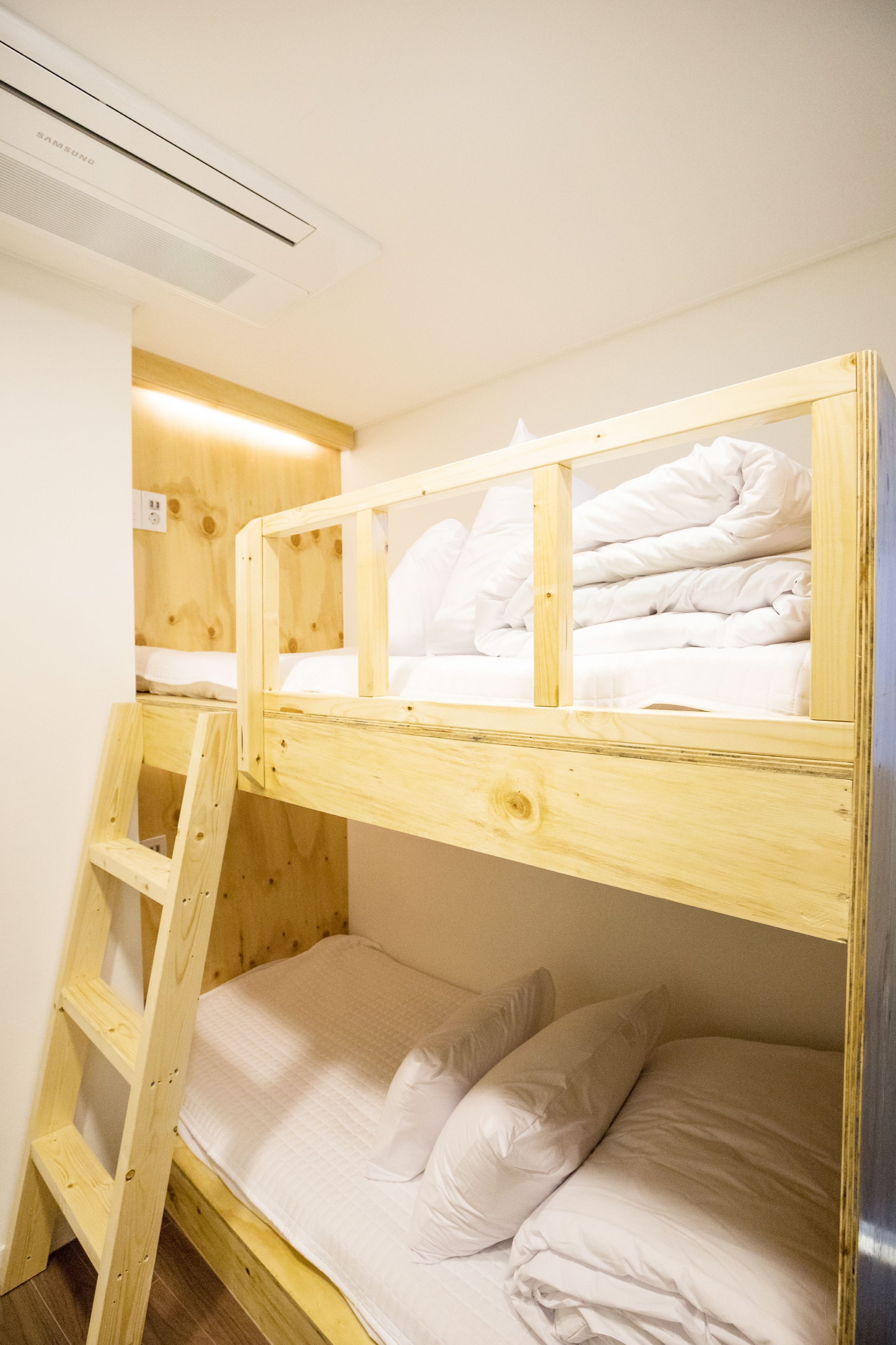 A bunk bed with a wooden ladder, white bedding, and a wall-mounted air conditioner.