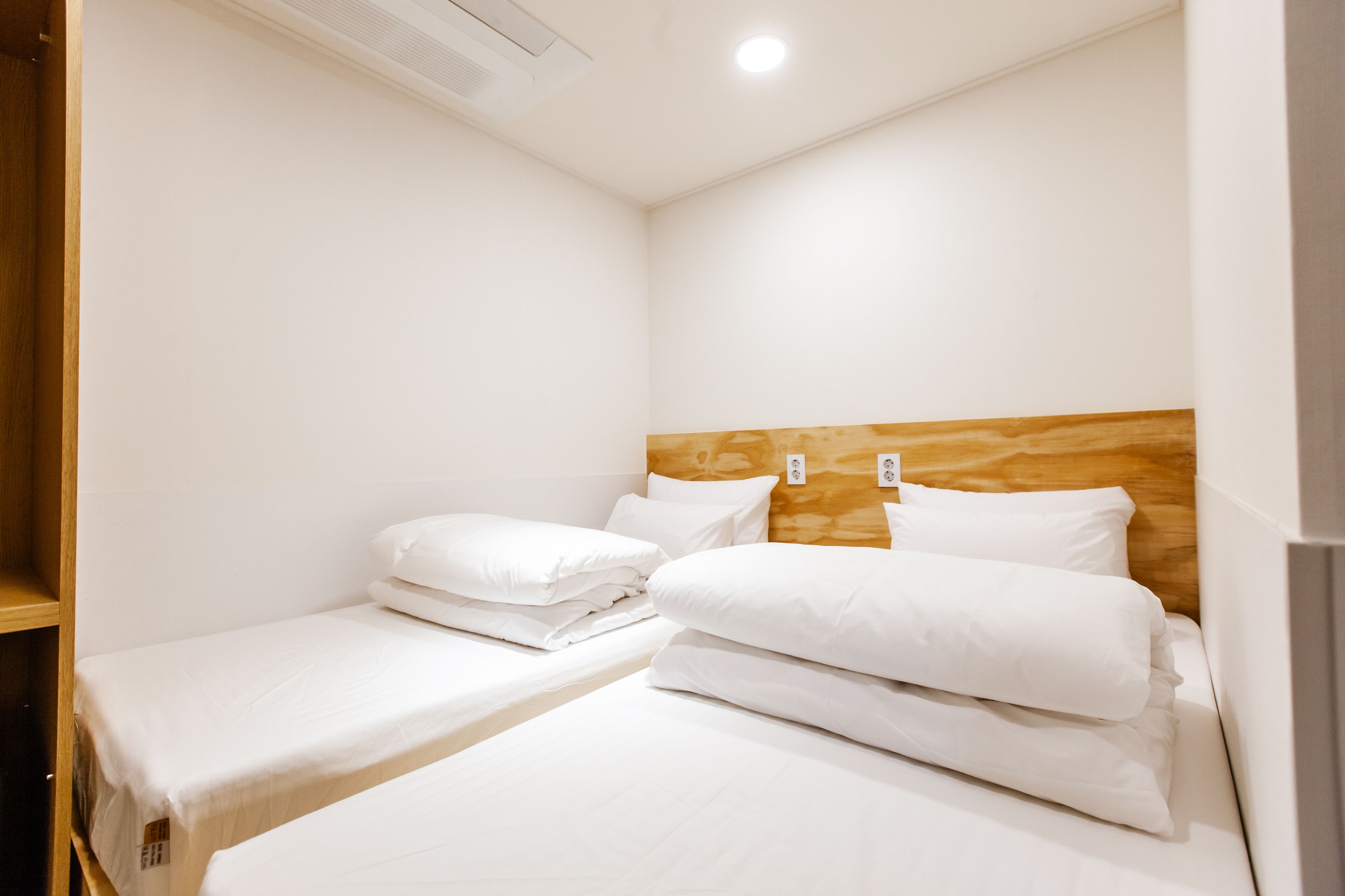 A hotel room with two single beds, a wooden headboard, and a small shelf.