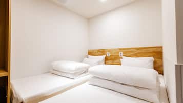 A hotel room with two single beds, a wooden headboard, and a small shelf.