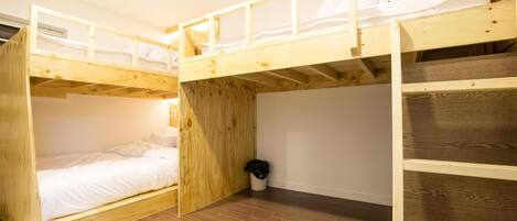 Habitación con literas de madera, un colchón blanco y un cubo de basura pequeño.