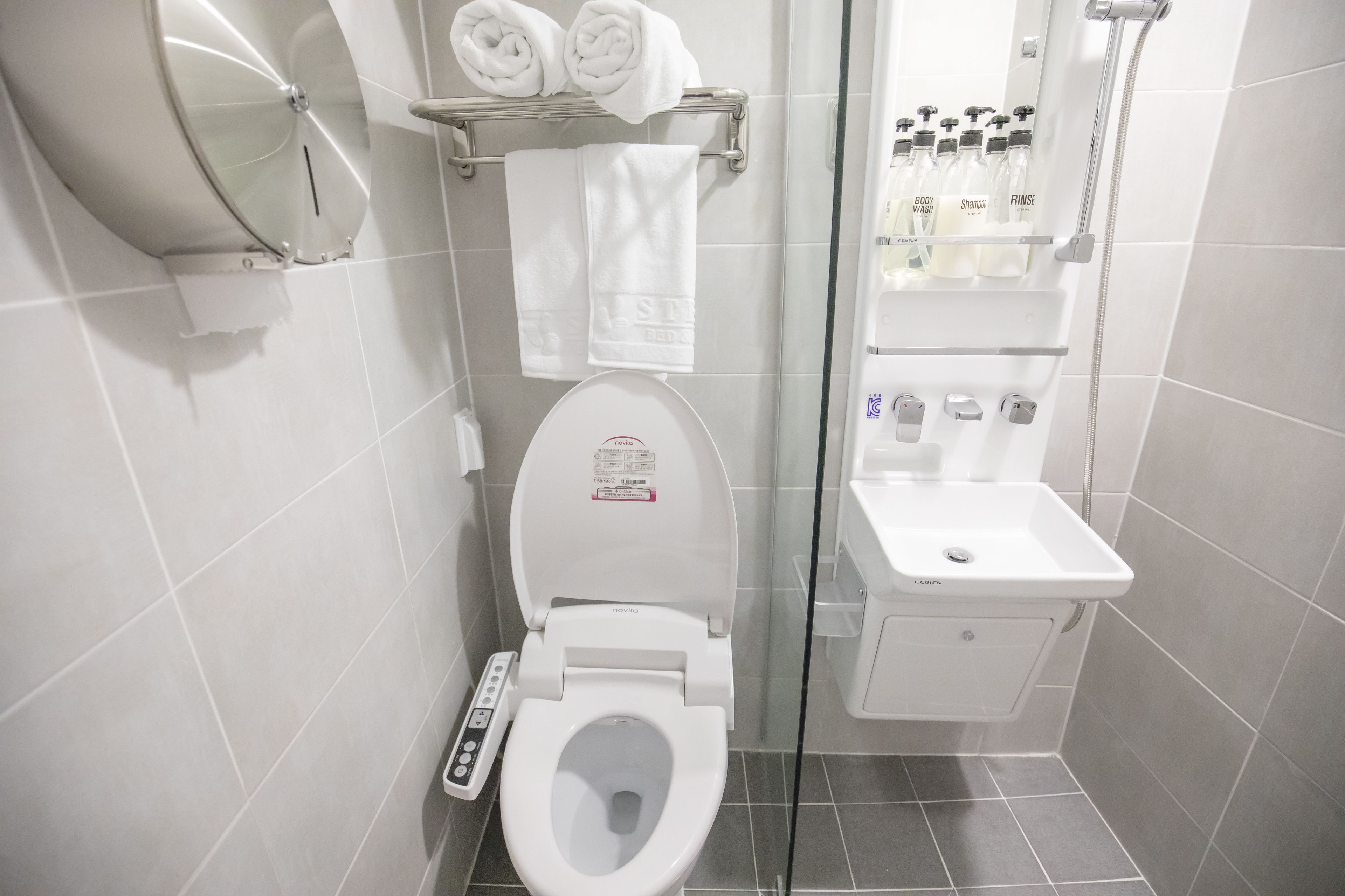 A modern bathroom with a toilet, a glass shower enclosure, and a shelf with toiletries.