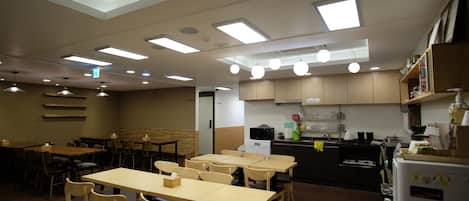 A restaurant with multiple tables and chairs, a kitchen area, and a ceiling with recessed lighting.
