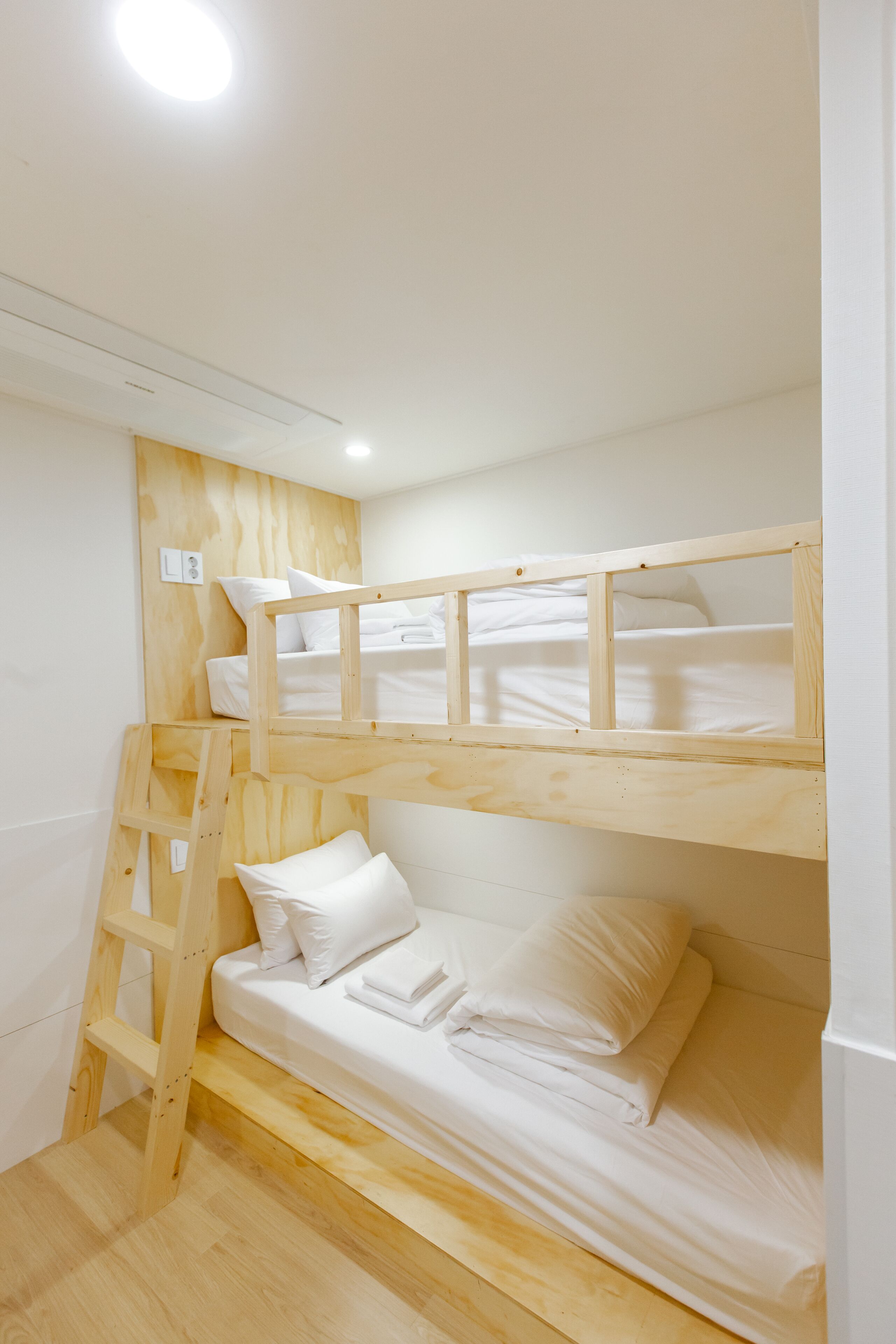 A bunk bed room with a wooden ladder, white bedding, and a white ceiling light.