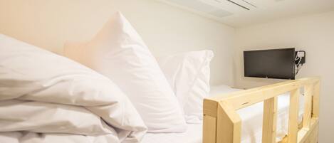A single bed with white bedding, a wooden headboard, and a television on the wall.