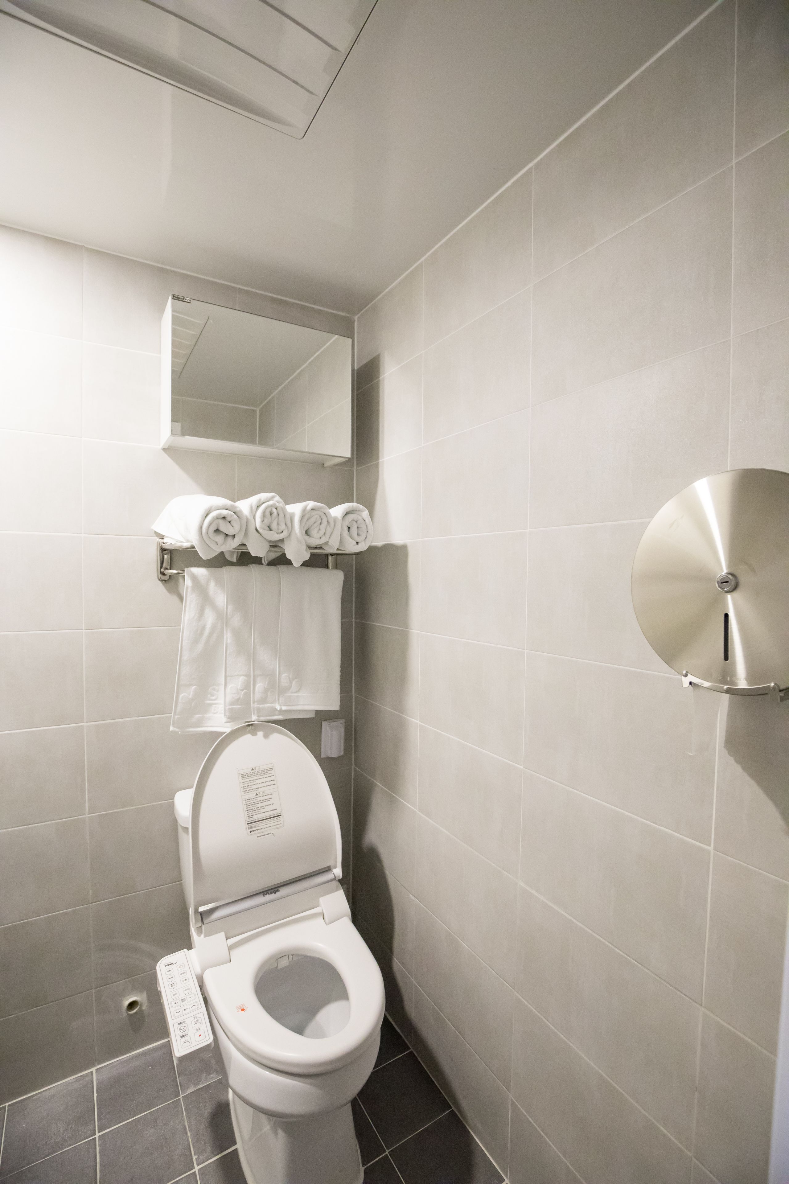 Un baño moderno con inodoro, toallero con toallas, espejo y dispensador de papel higiénico en la pared.