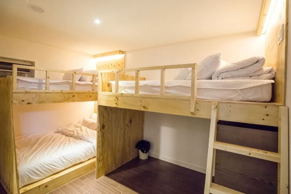 A bunk bed room with a wooden floor, a small window, and a wall-mounted light fixture.