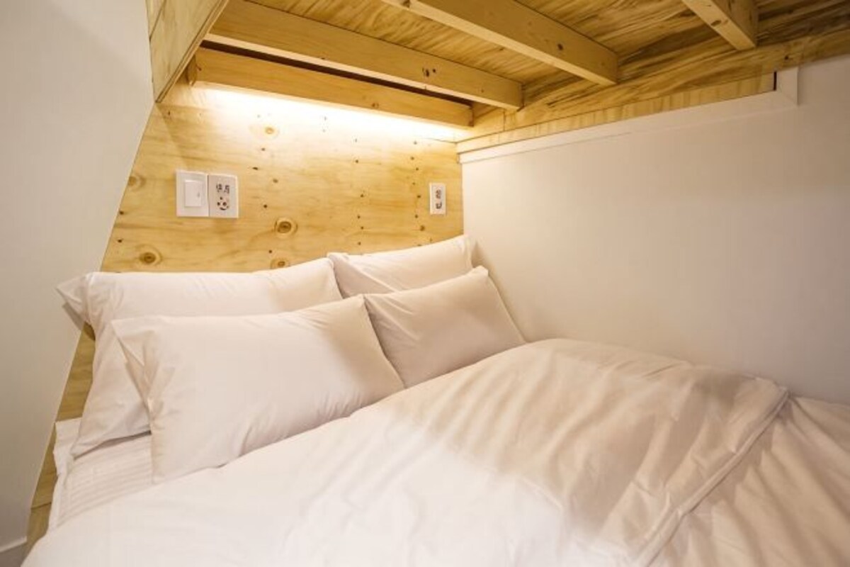 A bedroom with a wooden ceiling, a bed with white bedding, and a white wall.