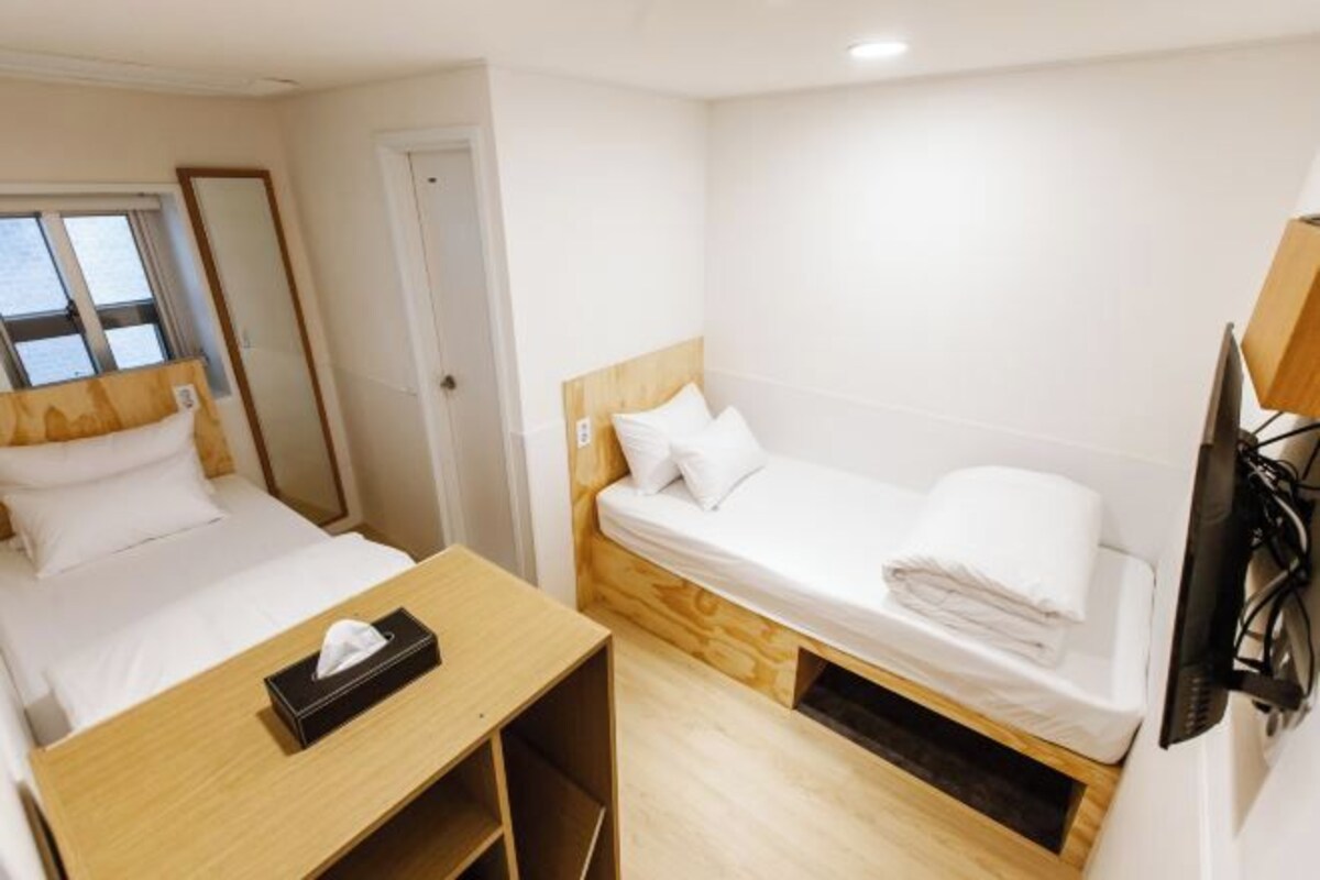 A compact hotel room with a single bed, a small desk, a TV, and a window.