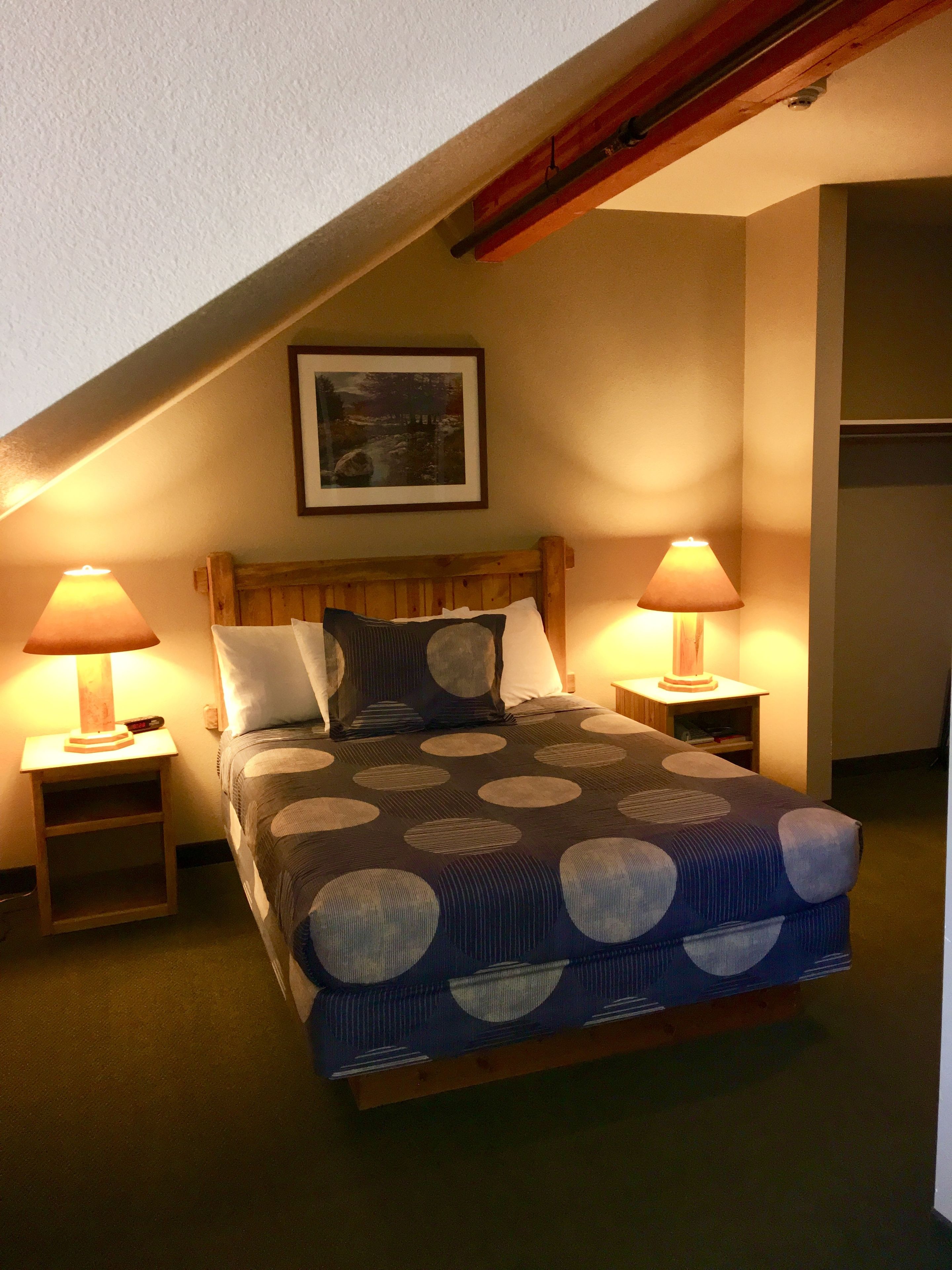 Une chambre à coucher comprenant un lit, deux tables de chevet, une commode, une tête de lit, un tableau accroché au mur et un plafond en pente.