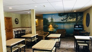 A restaurant with wooden tables and chairs, a mural of a lake, and a television screen displaying a menu. - Boulder Creek Inn (Donnelly)