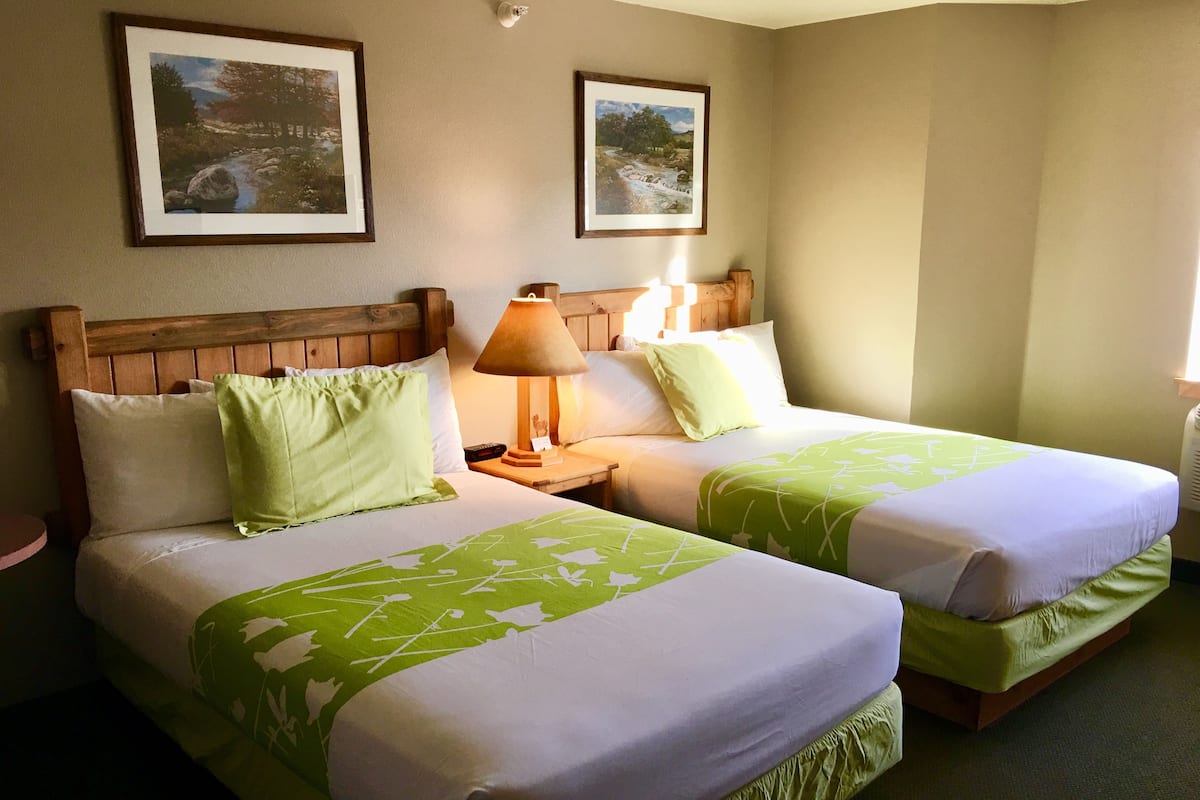 A hotel room with two beds, each with green and white bedding, wooden headboards, and framed pictures on the walls.