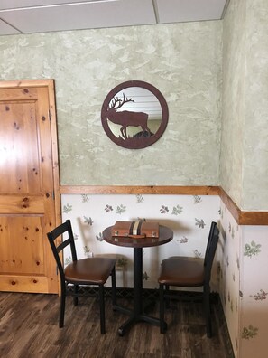 A corner of a room with a wooden cabinet, a round table with two chairs, and a wall with floral wallpaper.
