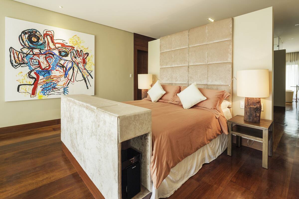 A modern bedroom with a large bed, two bedside tables with lamps, a marble bedside console, and a colorful abstract painting on the wall.
