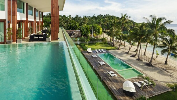 A modern hotel with a large swimming pool, lounge areas, and a view of the beach and ocean.