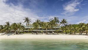 A beachfront hotel with a row of palm trees, a sandy beach, and a clear blue sky.
