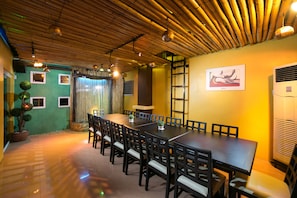 A dining area with a long table and chairs, a bamboo ceiling, and a green wall with windows. - 950 Condotel (Angeles City)