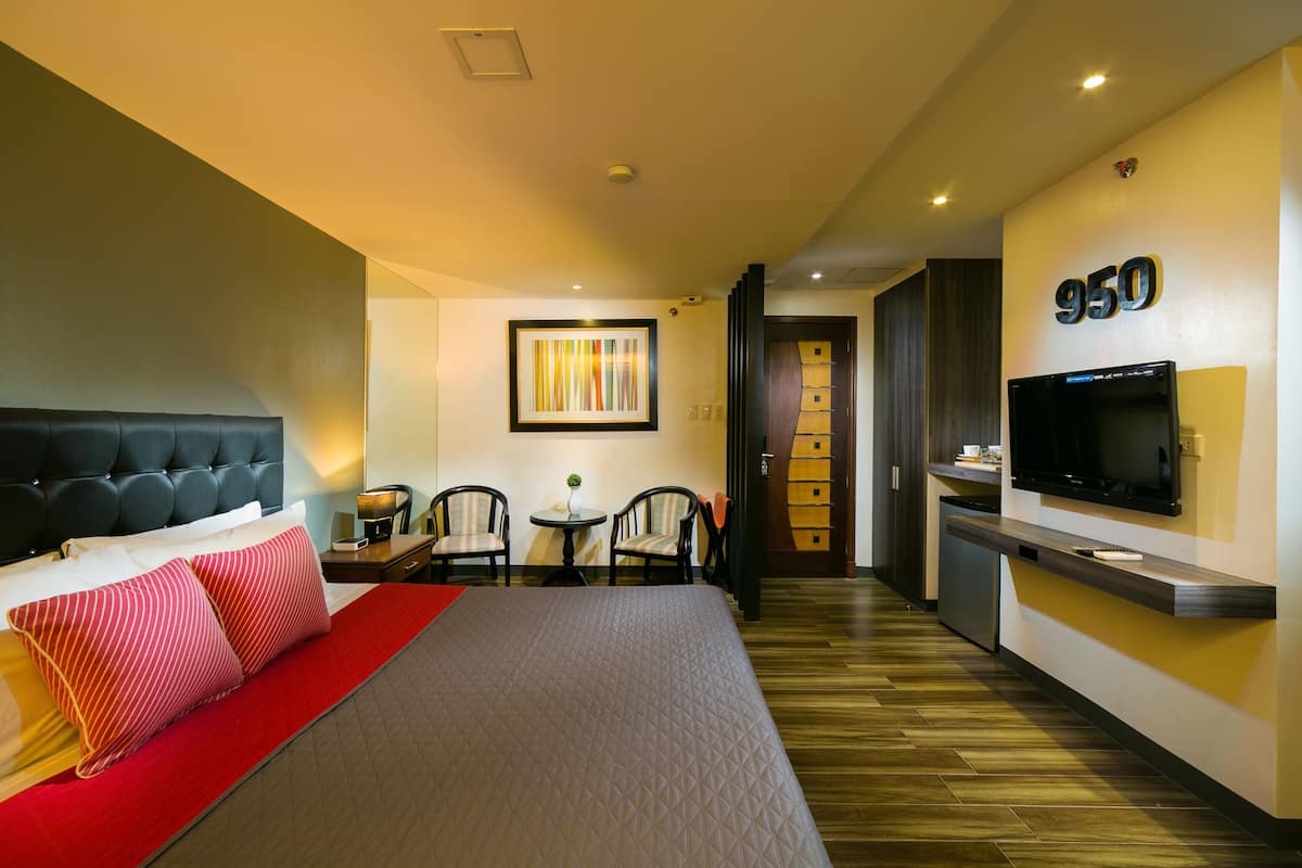 A hotel room with a bed, a TV, a desk with a chair, and a small table with a plant.