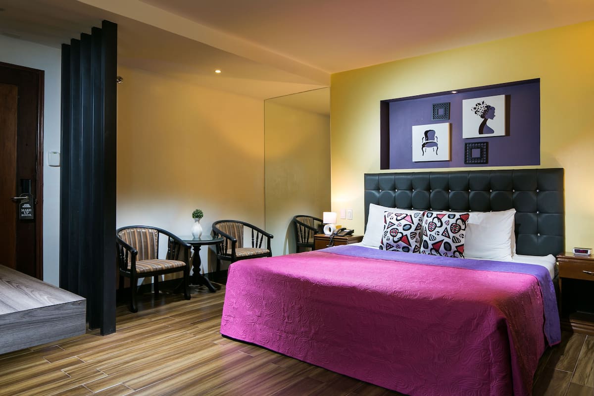 A hotel room with a large bed, a desk, two chairs, and a small table.