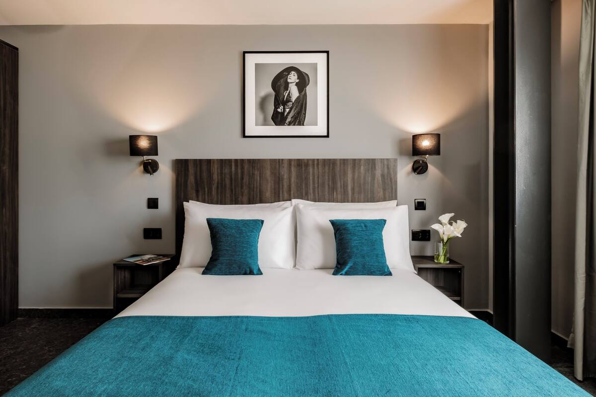 A hotel room with a large bed, two bedside tables, a framed picture on the wall, and a nightstand with a vase of flowers.
