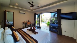 Habitación de hotel con una cama grande, un escritorio, una silla, un ventilador de techo y una puerta corrediza de vidrio a un área de piscina.