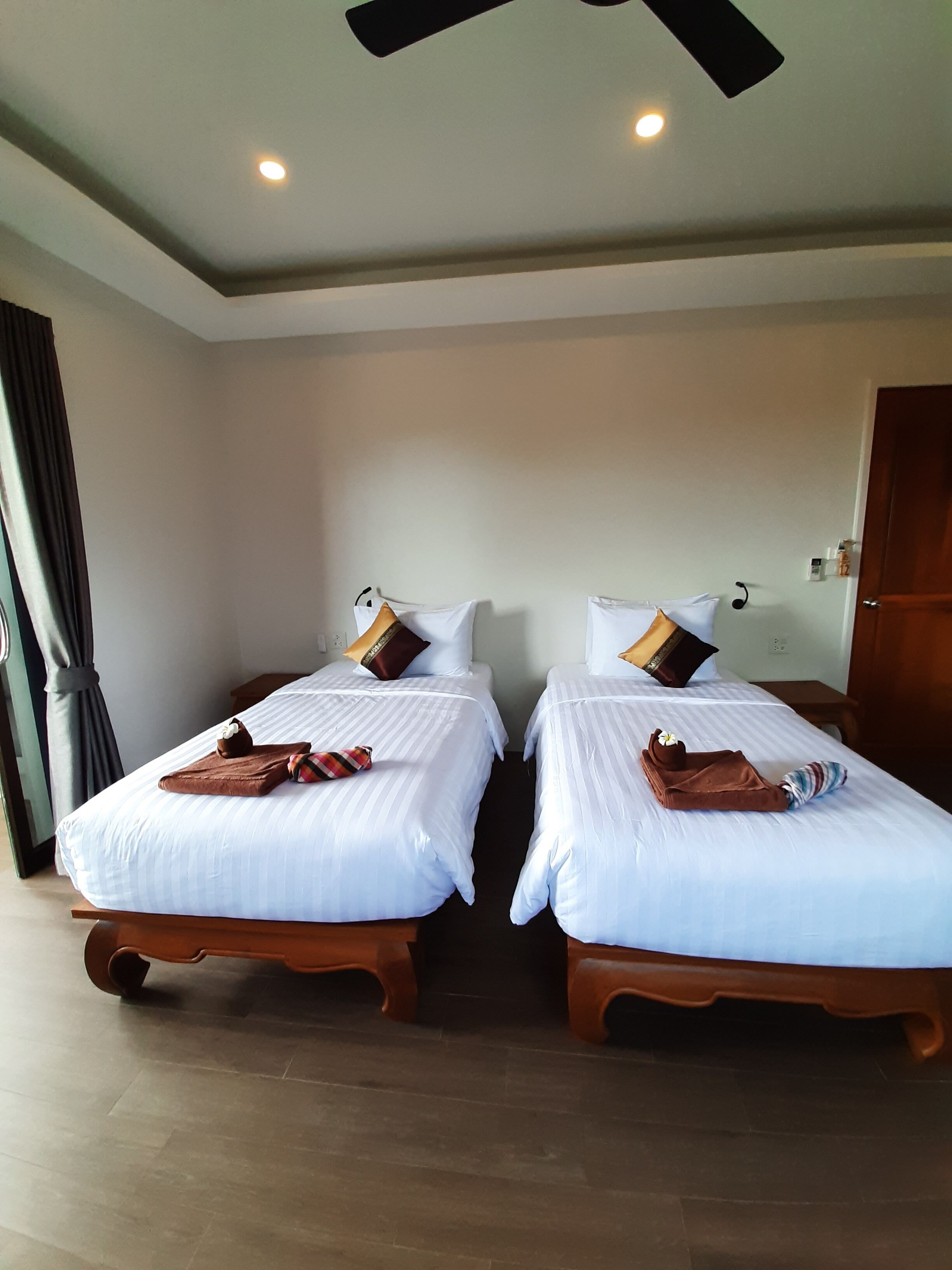 A hotel room with two single beds, each with a pillow, a brown towel, and a striped towel.