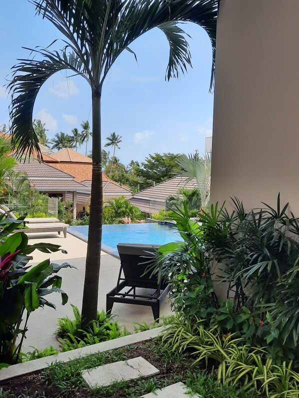 A poolside area with a lounge chair, palm trees, and a view of a building with a tiled roof.