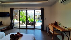 Habitación de hotel con cama, escritorio, televisión y vista al área de piscina exterior.