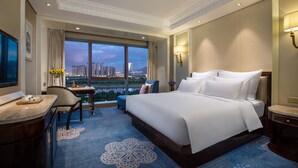 A hotel room with a large bed, a desk, a chair, and a view of the cityscape.