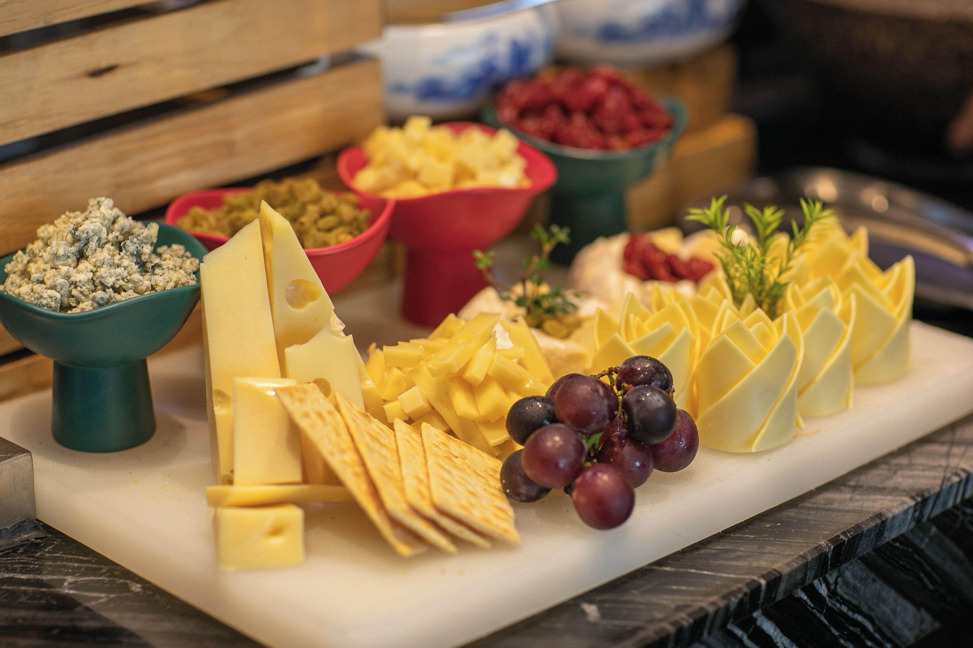 A cheese board with various cheeses, crackers, and grapes.
