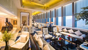 A spacious lobby with multiple seating areas, large windows, and a decorative staircase.