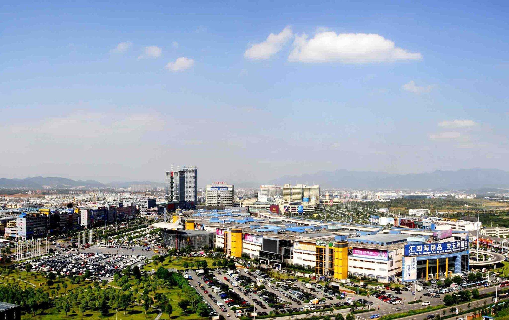 A cityscape with a mix of commercial and residential buildings, a large parking area, and a clear sky.