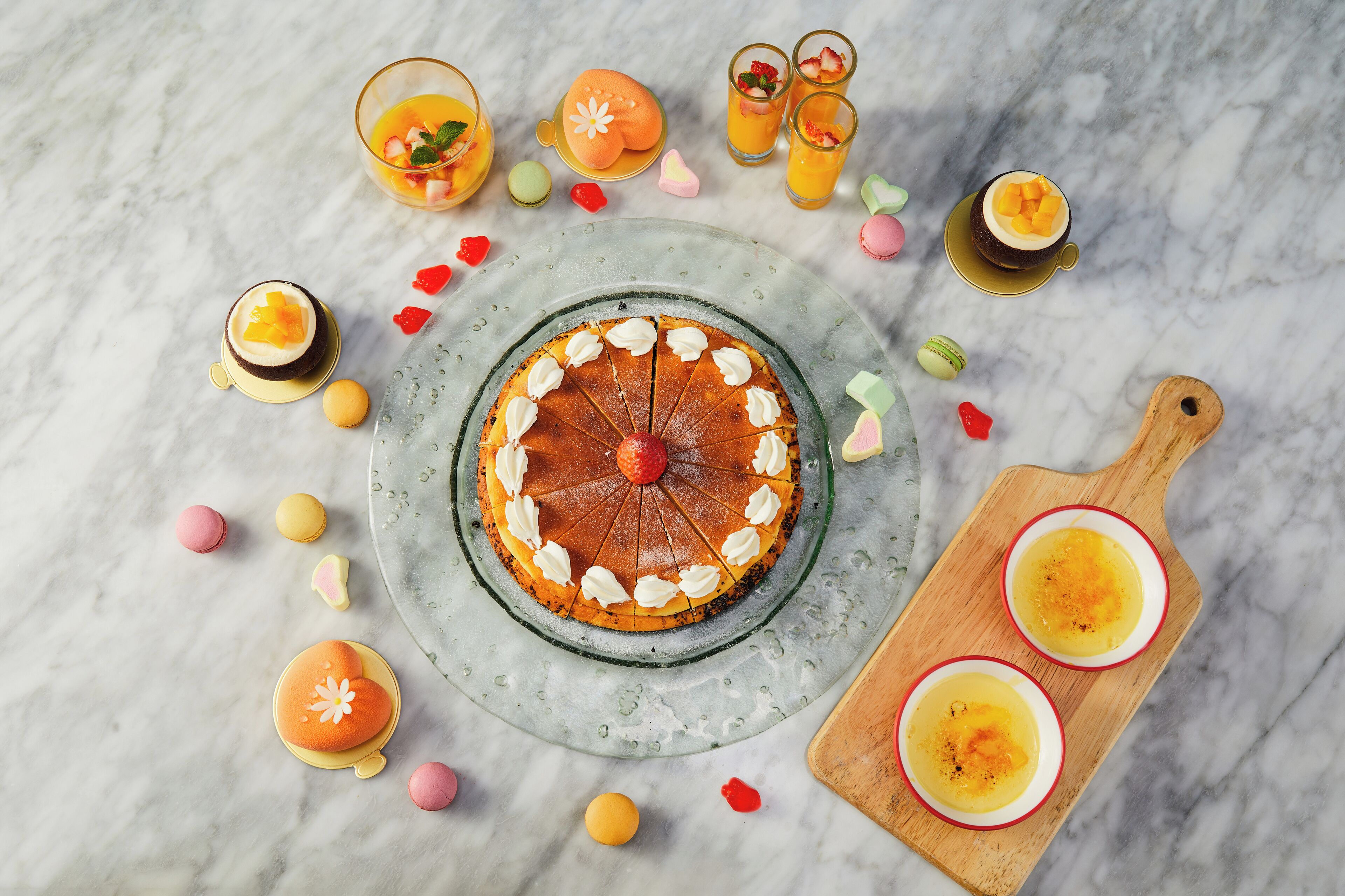 A dessert table with a cake, fruit, and drinks on a marble surface.