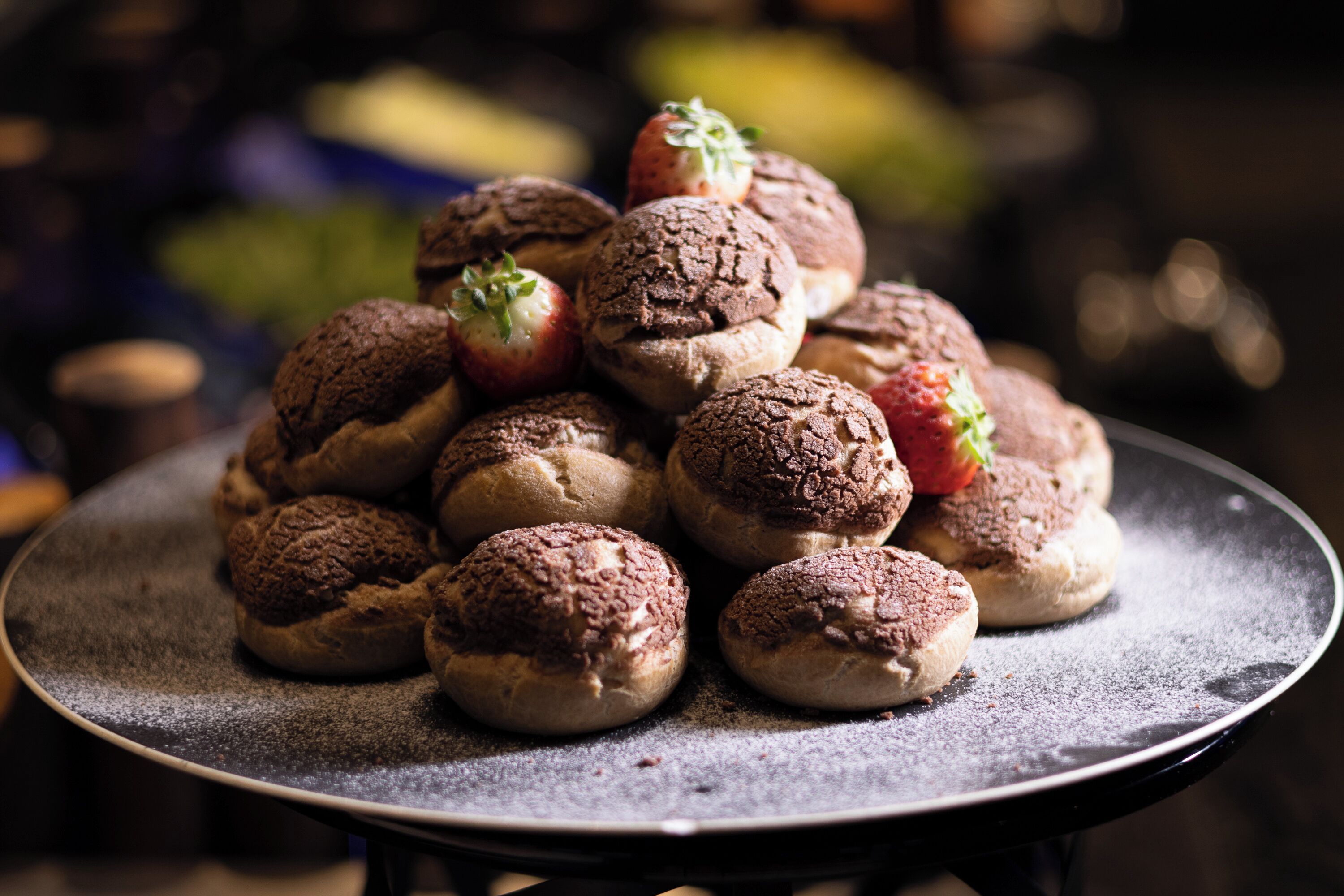 A tray of chocolate-covered buns with strawberries on a table.